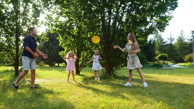 Happy cute family having fun weekend on nature. Wife and husband throwing frisbee disk in park while little children jumping cheering for parents. Summertime. Outdoor activity concept. Real time.