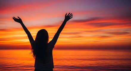 Fototapeta premium Silhouette of a woman with arms raised against a vibrant sunset over the ocean, symbolizing freedom, joy, and connection with nature