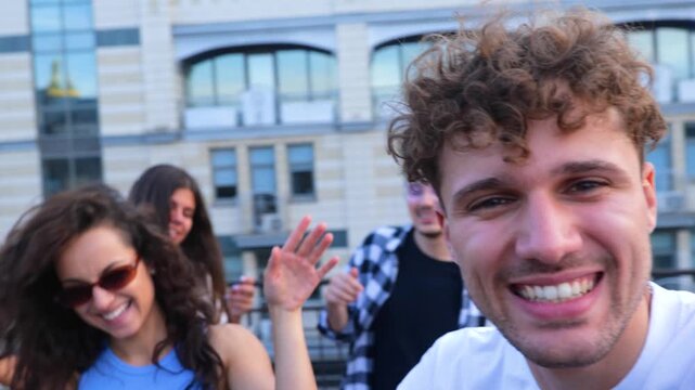 Happy man holding camera and filming friends party on rooftop. Young people dancing on roof terrace. Lifestyle, fun, open party concept. Real time