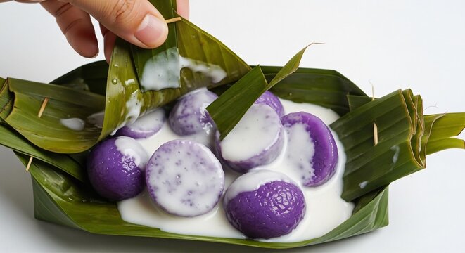 Hand opening a banana leaf wrap of Kue Bugis Mandi, soaked in thick white coconut sauce, plain white background.