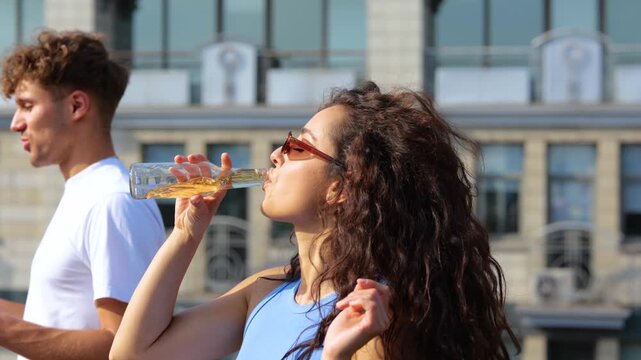 Pretty young female in sunglasses enjoying open air party on the roof terrace while dancing and drinking beer, friends next to her. Lifestyle, friendship, fun, open party concept. Real time