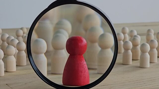 A magnifying glass and a red wooden figures with blur business man who search for someone who special person