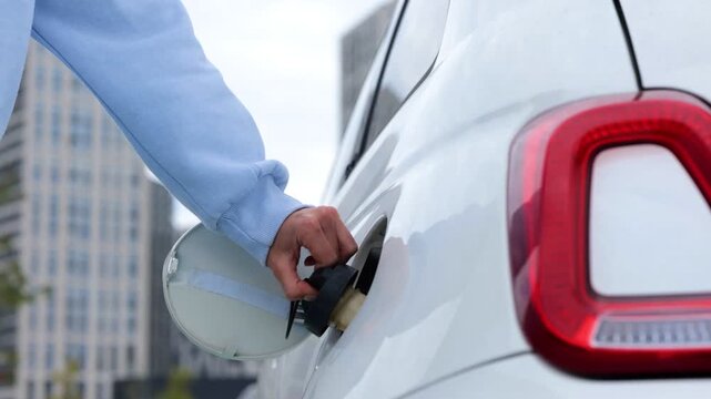 Close up of female hands putting charge cable into charging port in electric car outdoors in city. Real time video. Woman driver charges her electro vehicle at charging station. EV concept