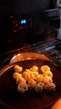 Cooked dumplings on black plate with rising steam. Hot meat dumplings served on dark plate with visible steam in blurred kitchen background.