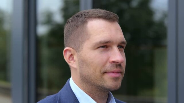 Close up of handsome young confident man in suit walking outdoors in city looking around. Caucasian successful businessman walks in street. Real time concept. Urban style, business concept.