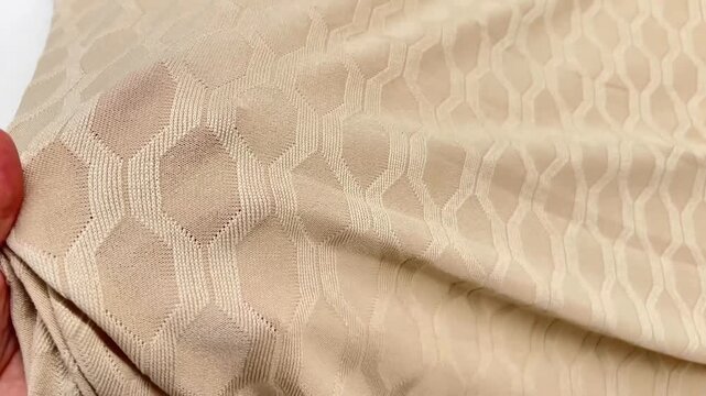 Creamy beige jersey knit textile features an intricate embossed geometric honeycomb design with a soft elastic drape and refined tactile surface for premium fashion apparel.