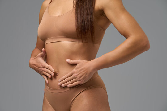 Fit woman in beige underwear touching her stomach and showing healthy belly