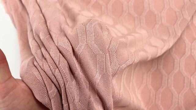 A detailed view of dusty rose jacquard jersey fabric reveals a raised hexagonal geometric pattern where the soft knit material is draped and folded to show the texture and fluid movement