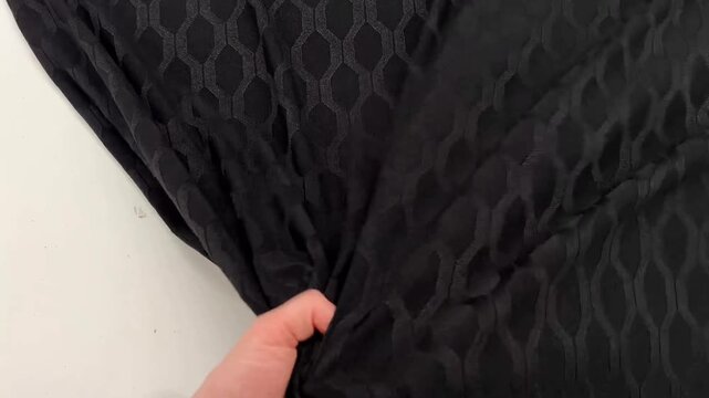 Soft black jacquard jersey material features a raised hexagonal knit pattern that creates a textured geometric surface while the fluid fabric drapes and folds to showcase its flexible structure.