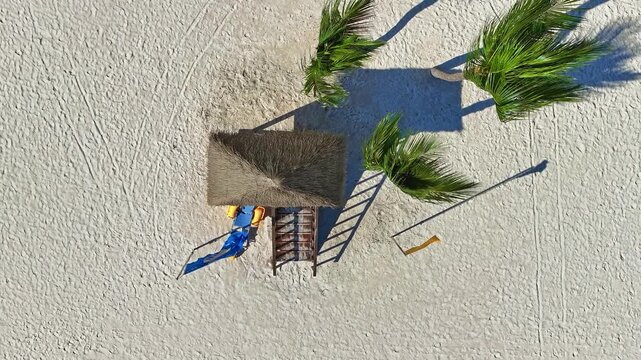 A wooden lifeguard tower with a thatched roof on white sand. Summer beach house with blue and yellow first aid flags to save lives of drowning people. Lifeguard tower on a Caribbean beach.