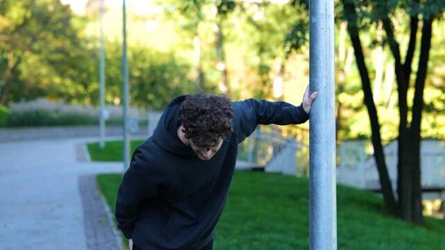 Young Caucasian man feeling pain after working out. Sportsman running in park, feeling leg hurt after outdoor activities. Face of guy showing strong pain. Real time.