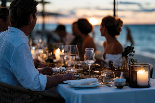 An elegant beach dinner setting showcasing a table adorned with fine dishes and decorative elements, offering guests a tasteful dining experience by the ocean at sunset.