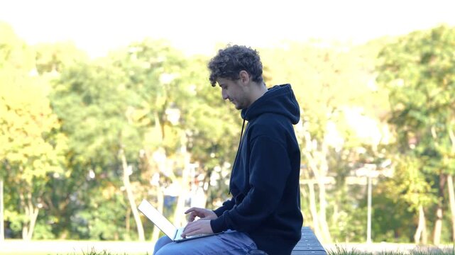 Smiling man drinking coffee and sitting on the bench in the park while working with laptop. Autumn season. Education, working concept. Real time concept.