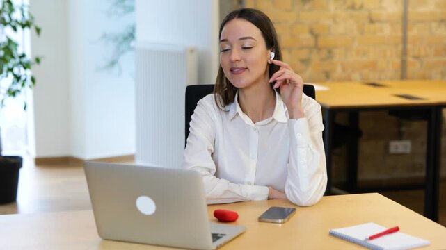 Realtime video, Relaxing work in the modern office. Caucasian beautiful woman is sitting in front of her laptop and meditating, woman is smiling and listening to music.