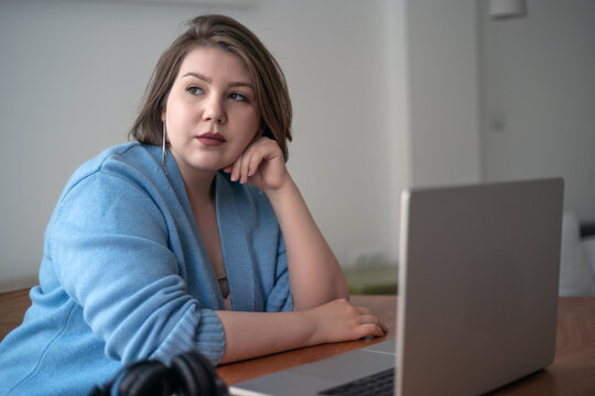 Remote work plus size woman using laptop in home office, thoughtful freelancer, body positivity, online learning, modern workspace lifestyle.
