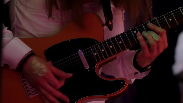Professional guitarist wearing white shirt plays melodic sequence on orange electric guitar with black pickguard during live concert performance