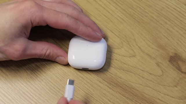 Man charging white wireless earbuds in a charging case.