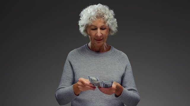 Senior lady is counting usd paper money. Old woman holds cash dollars in hands, calculates a loan or mortgage. Retired female invests, counts the remaining savings 100 banknotes, economic crisis.