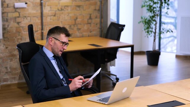 Realtime video. Caucasian man in black suit is sitting and ridding papers, woman in white shirt is coming to room, and sitting down at table.