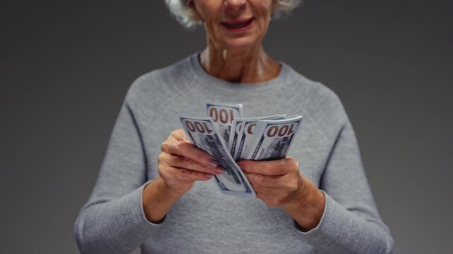 Senior lady is counting usd paper money. Old woman holds cash dollars in hands, calculates a loan or mortgage. Retired female invests, counts the remaining savings 100 banknotes, economic crisis.