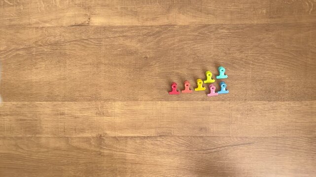 child hands placing seven small colorful clips in a row on wooden table slow motion 4K