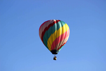 Naklejka premium Diagonal rainbow striped hot air balloon floating in clear blue sky