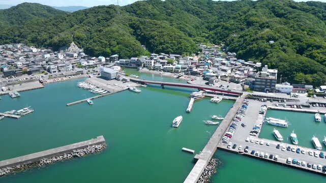 Aerial drone view of small fishing harbor with red bridge and boats in coastal village in Wakayama, Japan