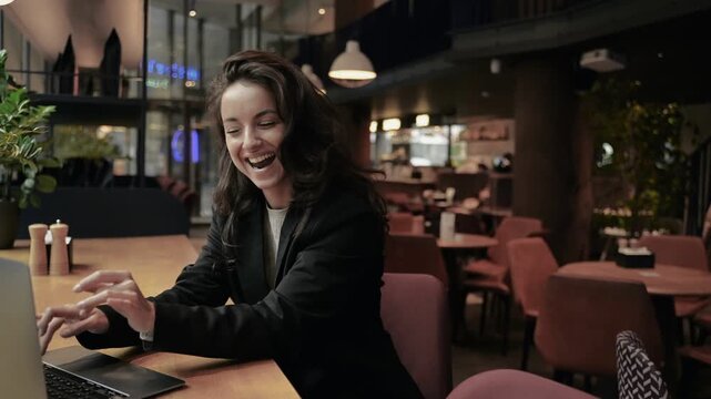 Happy satisfied woman using laptop while sitting at cafe and working. Lady screaming happily. Motivation with an attractive young female entrepreneur at work online. Real time