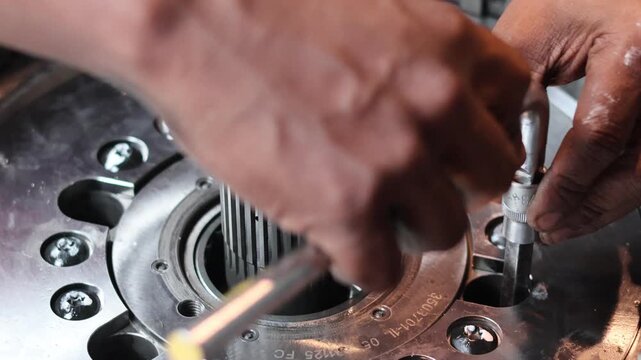 A professional static shot of a mechanic's hand using a hex key socket to tighten bolts inside a heavy-duty industrial gearbox.
