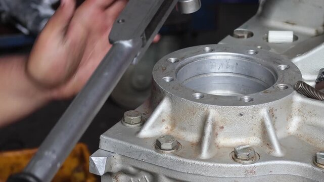A medium static shot showing mechanics working together to assemble or repair a heavy industrial gearbox. One technician is using a torque wrench.