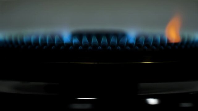 Close up gas stove burner igniting with blue flame on dark background, kitchen cooking heat, fire ignition detail, energy concept for culinary, home improvement and instructional video backdrop