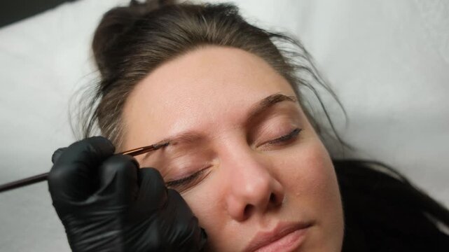 Professional cosmetologist coloring client's eyebrows with henna dye in a modern beauty salon