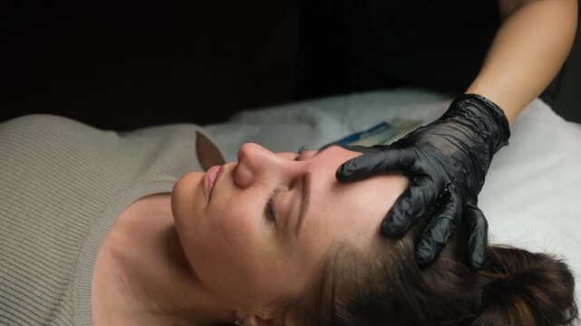 Beautician in black gloves tweezing the eyebrows of a female client in a beauty salon
