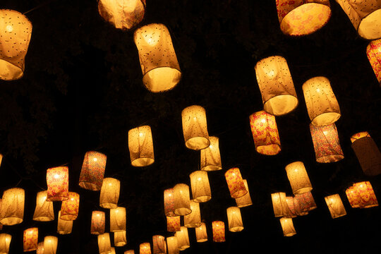 Warm glowing paper lanterns hanging in dark night sky, festive illumination and cultural celebration atmosphere with soft golden light