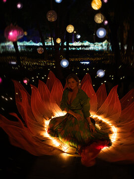 Woman sitting inside glowing lotus flower light installation at night, spiritual meditation and feminine energy concept