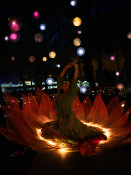Woman sitting inside glowing lotus flower light installation at night, spiritual meditation and feminine energy concept