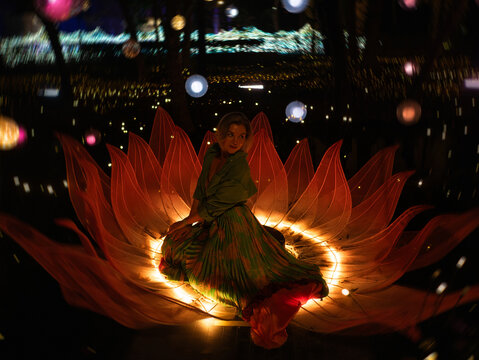 Woman sitting inside glowing lotus flower light installation at night, spiritual meditation and feminine energy concept