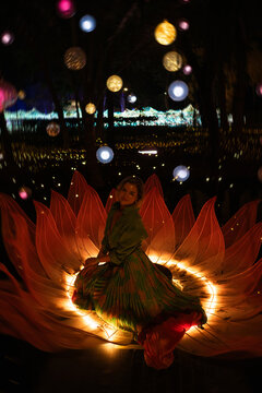 Woman sitting inside glowing lotus flower light installation at night, spiritual meditation and feminine energy concept