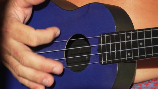 Ukulele hand music, close-up playing blue instrument, strumming strings