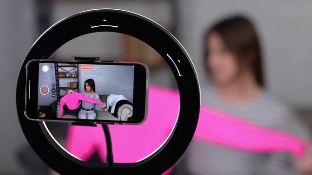Female vlogger using mobile phone while recording video for sell clothes, selling online. Lady showing jumper at home office. Small business owner, online market concept. Real time video.