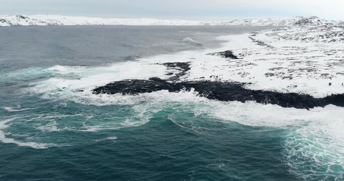 Drone footage captures the contrast between icy land and restless sea along a remote northern coast.