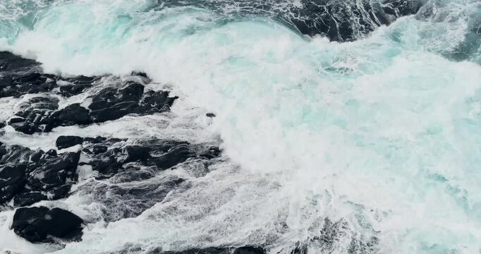 Aerial drone shot of turbulent sea water colliding with icy coastal rocks in winter.