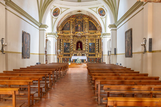Chapel interior presenting an elaborate golden altarpiece and rows of traditional wooden benches in arguedas, spain