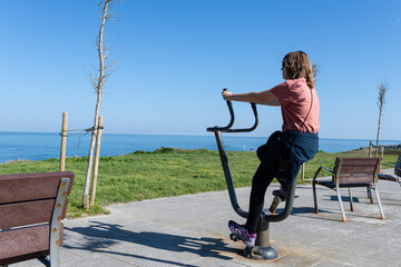 Obraz premium Woman performing physical activity on public exercise machine along the coast