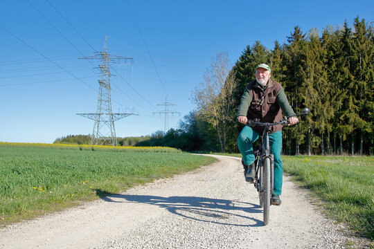 Active senior riding e-bike on rural path with high voltage power lines in the background, concept of sustainable energy and modern mobility.