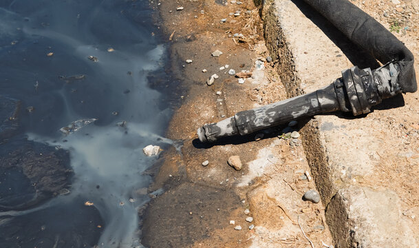 black industrial nozzle discharging murky, greyish liquid onto a wet ground surface