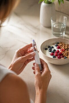 Hands holding injection pen near healthy breakfast bowl, diabetes management, medical routine, healthcare and nutrition concept.