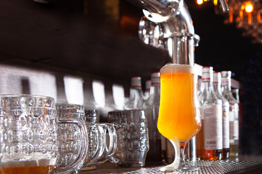 Beer is poured into tall glasses. Beer taps in pub are made of shiny steel. Vintage style. Concept of vacation or party. Frothy alcoholic drink. Bar equipment
