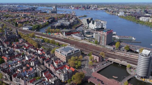 Westerdok district of Amsterdam revealing train tracks of central station, canal boats navigating river IJ, urban cityscape with historic and modern architecture
