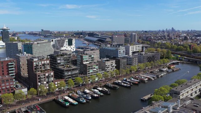 Westerdok district in Amsterdam revealing modern architecture, houseboats along canal, city skyline with Central Station, A'DAM Tower, and River IJ from aerial